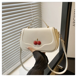 Macro shot of a cream-white crossbody bag with unique 3D red cherry metal decoration