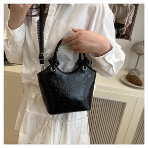 Detail of black bucket bag featuring embossed cartoon patterns and adjustable shoulder strap