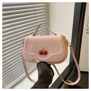 Detail of pink crossbody bag featuring a 3D red cherry buckle and smooth texture