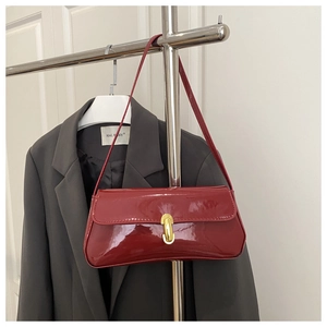 Detail of red patent leather underarm bag featuring a golden oval lock on a gray suit