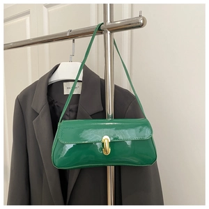 Green patent leather baguette bag with a gold metal clasp shown on a blazer