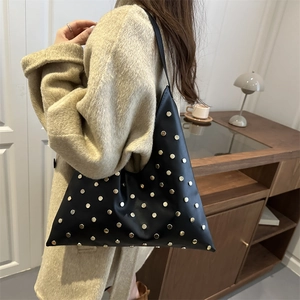 Sac à bandoulière chic en cuir noir mat avec rivets dorés dans un cadre urbain
