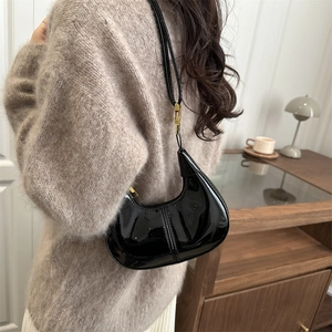Glossy black patent leather crescent hobo bag with adjustable gold buckle on a model