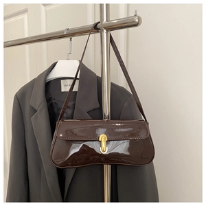 Detailed close-up of dark brown patent leather shoulder bag with gold capsule clasp