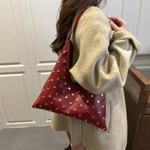 Sac hobo rouge moderne avec clous argentés et bandoulière en cuir sur un manteau