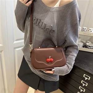 Brown leather crossbody bag with cherry decor worn by a model in a casual indoor setting