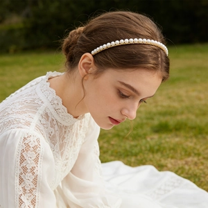 Elegant white pearl headband on gold metal frame worn by a model in outdoor setting