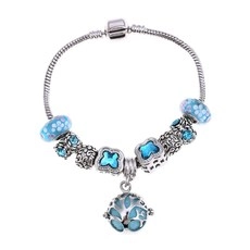 Detalle de cuentas de cristal azul y dijes de trébol en pulsera de cadena de plata
