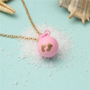 Detail view of a pink harmony ball pendant with gold baby footprints on beach sand