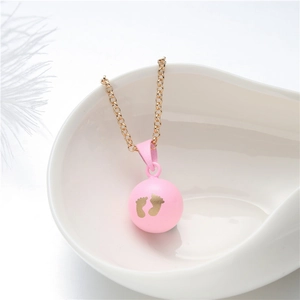 Detailed shot of pink pregnancy chime ball with golden baby footprints on a white bowl
