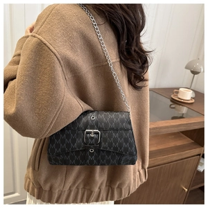 Detail of a black crossbody bag with M-pattern print and silver chain strap on a brown coat