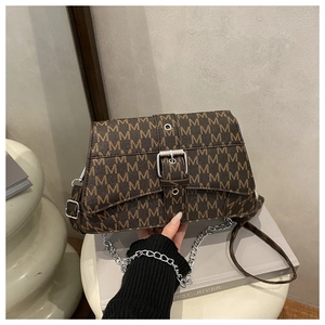 Macro view of M-letter print texture and silver buckle on brown leather crossbody bag