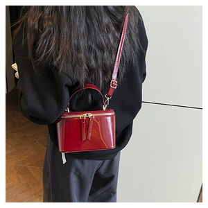 Detail view of a luxury red patent leather handbag with top handle and golden zippers