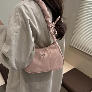 Pink glossy baguette bag with metal bow detail worn by model in light beige coat