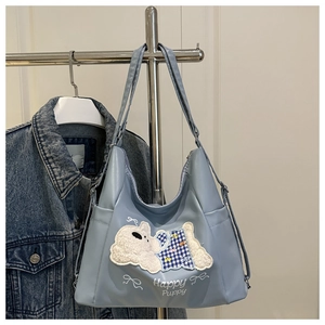 Detail of light blue tote bag with puppy embroidery and white ribbon print hanging