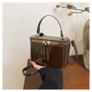 Close-up of a glossy dark brown patent leather box bag with gold metal zippers and handle