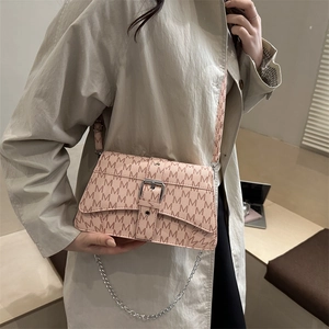 Pink crossbody bag with M-letter print and silver chain strap worn with khaki trench coat