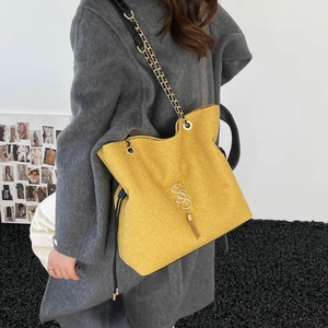 Gelbe Wildleder-Shopper-Tasche mit Kettenriemen und Quasten zum grauen Mantel getragen