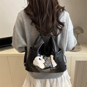 Fashionable black faux leather backpack with white fluffy puppy patch on back of model