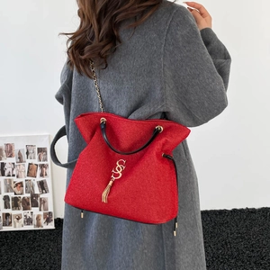 Rote Tragetasche mit goldenem S-Logo und Kettenriemen am grauen Wollmantel-Modell