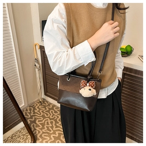Close-up of a brown patchwork crossbody bag with a cute white puppy plush keychain charm