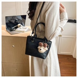 Dettaglio della borsa tote in tela nera e pelle con un dolce ciondolo a forma di cane
