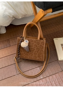Close-up of leopard print tote bag with plush charm and braided strap on wooden floor