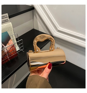 Detail of gold cylindrical evening bag featuring a unique curved handle and chain strap