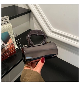 Close-up of black glossy cylinder handbag featuring a unique heart-shaped top handle