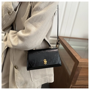 Close-up of a vintage black textured leather shoulder bag featuring a gold metal buckle