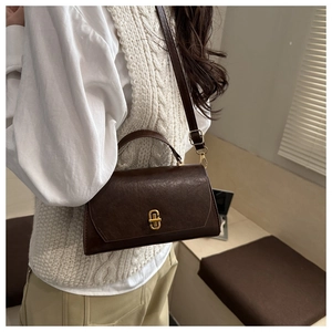 Detail of dark brown vintage shoulder bag with golden buckle worn by a model