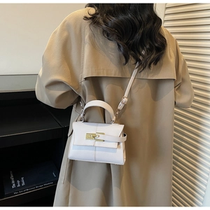 Close-up of a white mini Kelly bag with gold lock hardware on a trench coat background
