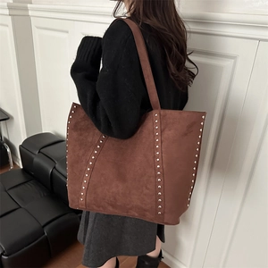 Sac cabas en daim marron avec clous argentés porté par un mannequin en studio
