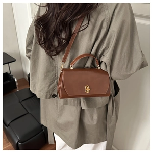 Detail of a brown vintage leather crossbody bag with a gold buckle on an autumn coat