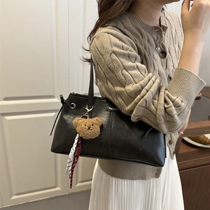 Vintage black tote bag with plush bear charm and fashion label on matte leather