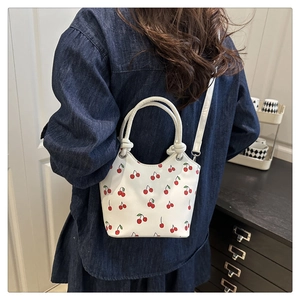 Detail of white cherry print handbag worn with denim jacket in a lifestyle setting