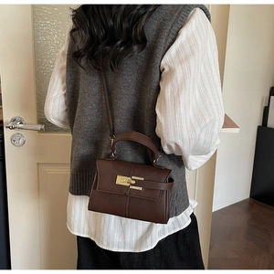 Close-up of a retro brown crossbody bag with litchi texture and golden metal swivel lock