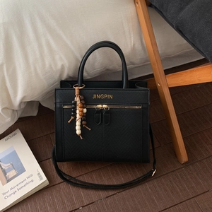 Detail of black leather tote bag with gold lettering and colorful beaded pendant