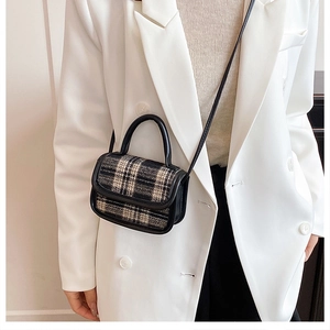 Detail of a chic black and white plaid tweed crossbody bag with black handles and shoulder strap