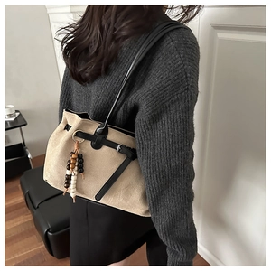Detail einer beigen Shopper-Tasche aus Wildlederimitat mit Lederriemen und Perlenanhänger