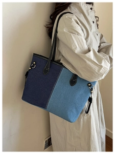 Detail of blue denim patchwork tote bag with black leather handles and metal hardware