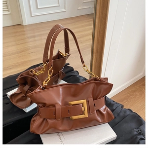 Détail des plis en cuir caramel et de la grande boucle en métal doré sur le sac fourre-tout