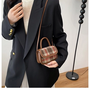 Close-up of a vintage plaid crossbody bag with brown leather trim worn by a model