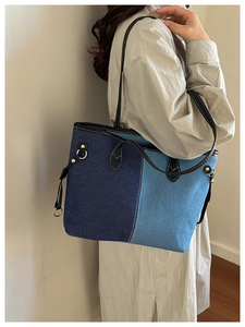 Detail of a large denim tote bag featuring contrasting blue panels and black leather trim