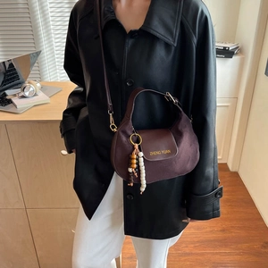 Brown suede half-moon crossbody bag with decorative tassels and metallic ring detail