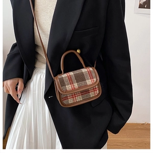 Close-up of retro plaid handbag with brown leather trim held by model in casual outfit