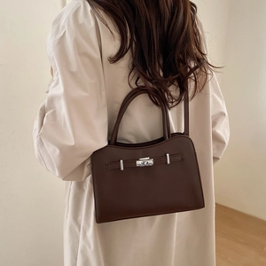 Minimalist dark brown leather crossbody square bag with silver buckle worn on a beige coat