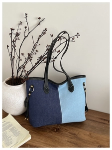 Détail du sac cabas en denim bicolore avec anses en cuir noir sur table en bois