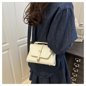 Close-up of a white textured crossbody bag with gold buckle on a model in a cozy room