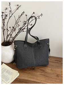 Détail d'un sac cabas en denim gris foncé avec surpiqûres blanches et garniture en cuir